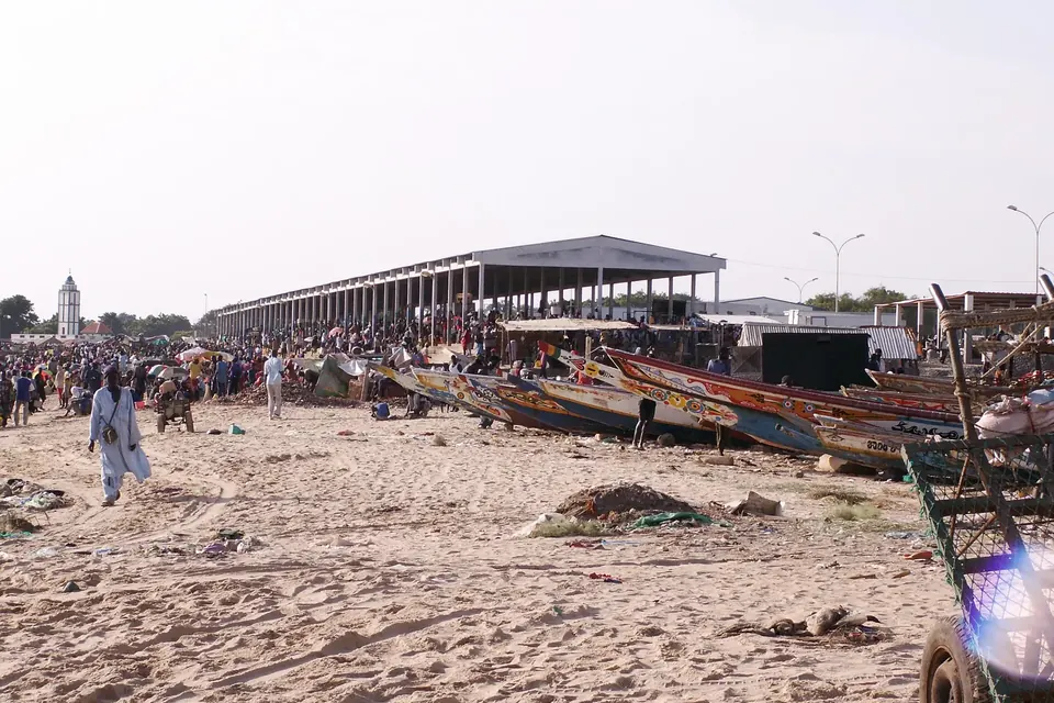 La jetée de pêche de Mbour au Sénégal, avec des pirogues échouées sur la plage et un bâtiment blanc où le poisson est découpé